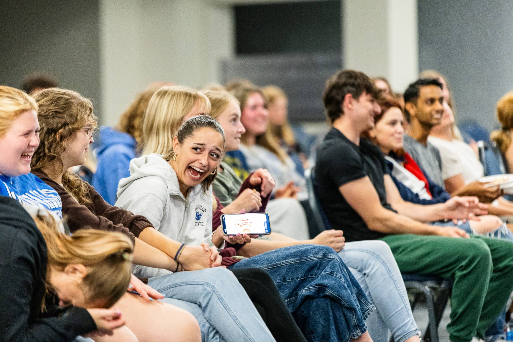 students sitting in chairs watching a performance and laughing